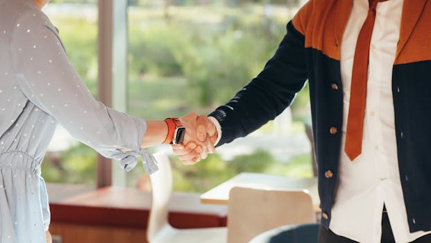 Close-up of colleagues shaking hands in an office, symbolizing teamwork and collaboration.
